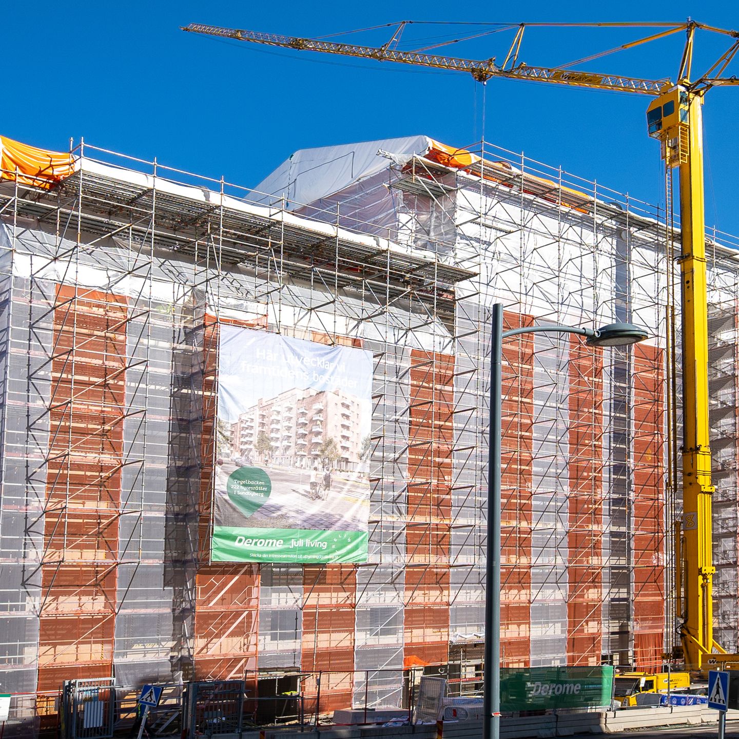 Hus i Tegelbacken i Sundbyberg med ställning, väderskydd och gul byggkran under byggnationen